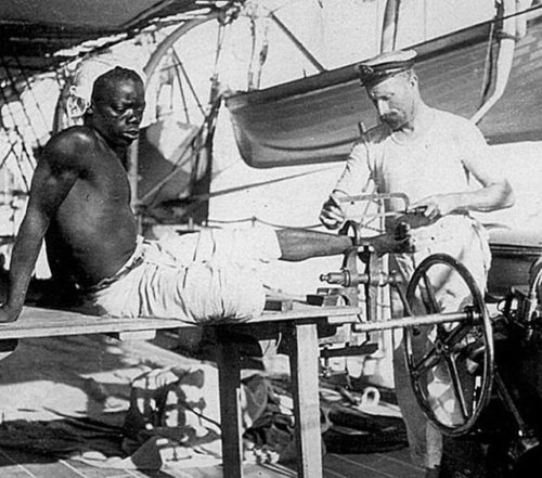 British sailor removing leg irons from slave. Late 1800s.